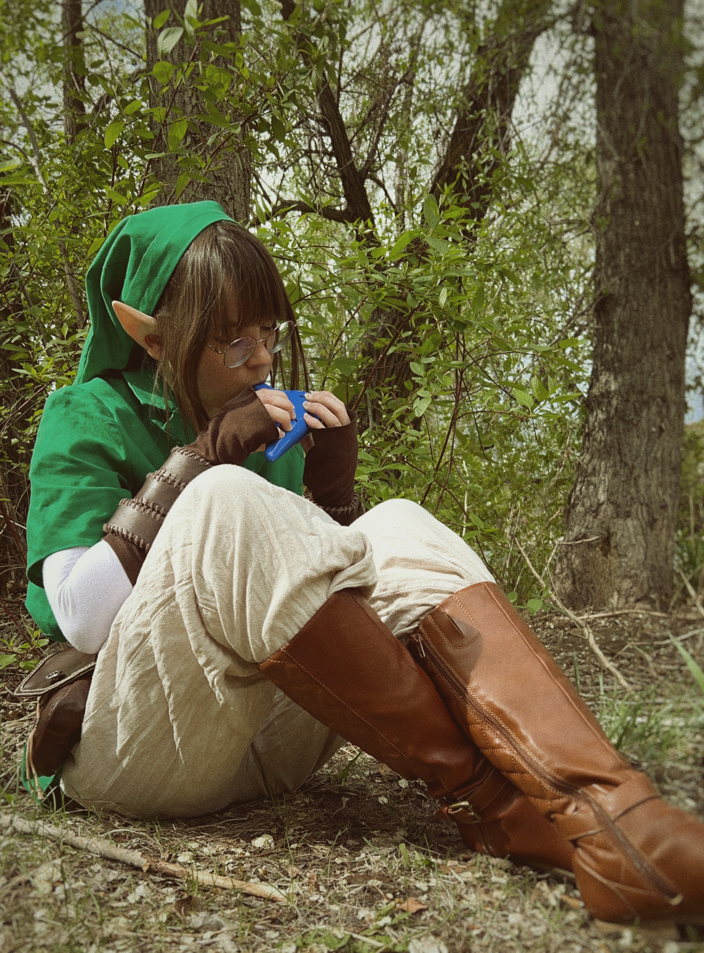 girl with brown hair, pointy ears, and glasses in green tunic and brown boots playing ocarina
