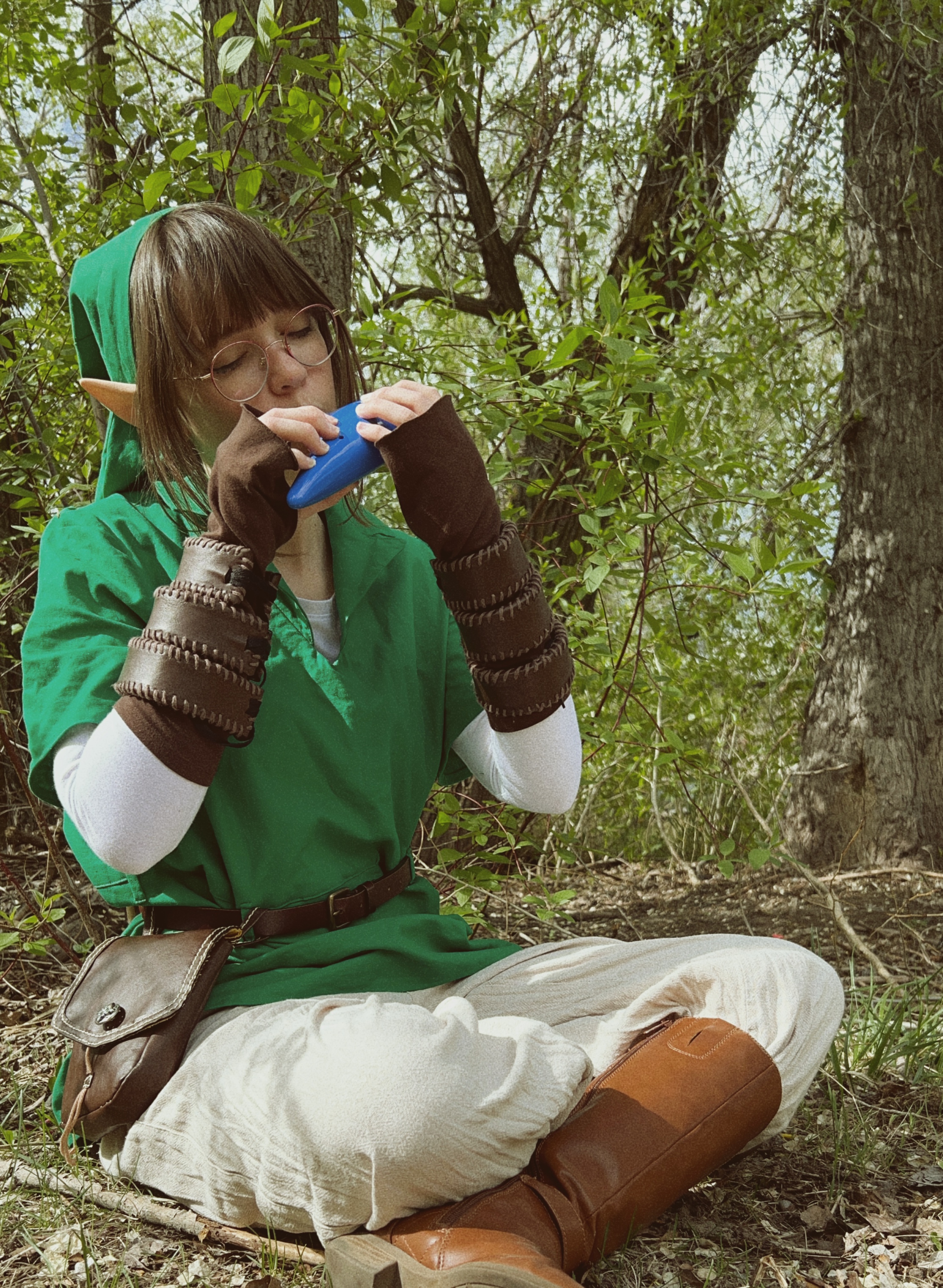 girl with brown hair and glasses in green tunic and brown gloves playing ocarina