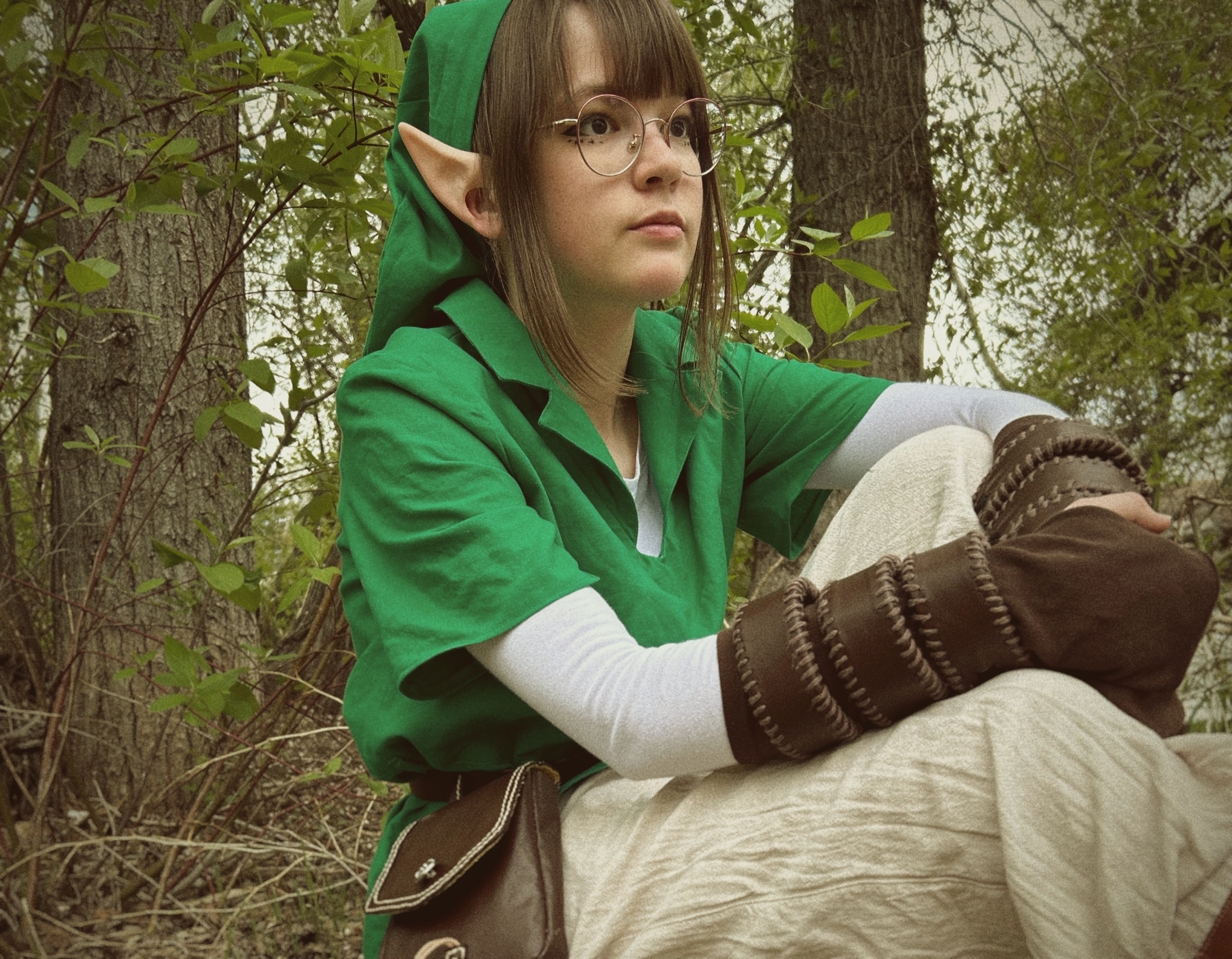 girl with brown hair, pointy ears, and glasses in green tunic and brown gloves
