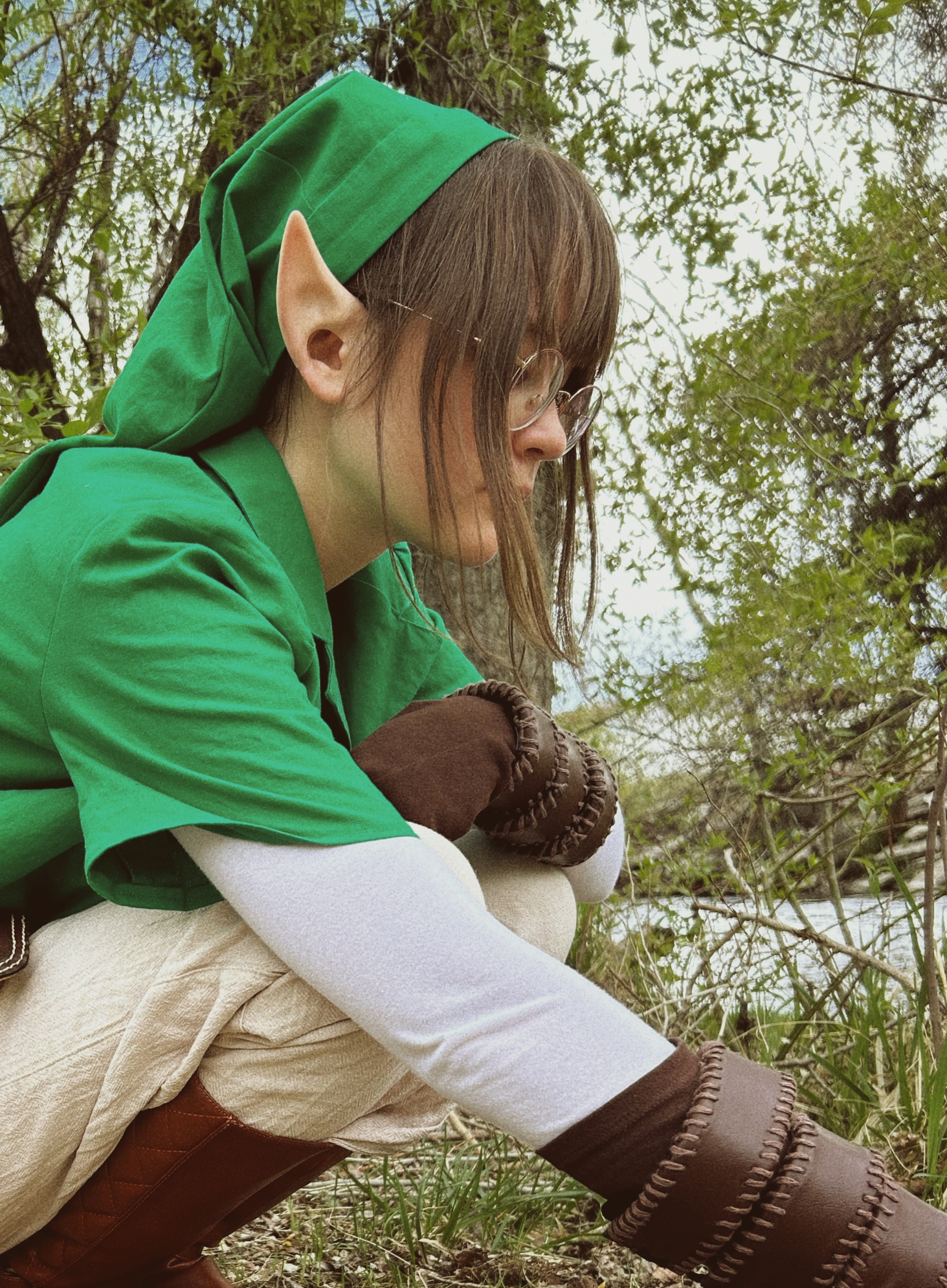 girl with brown hair, pointy ears, and glasses in green tunic looking at something on ground
